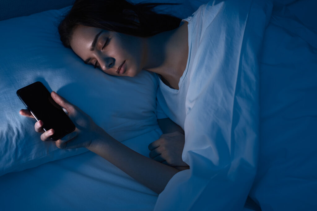 Stiligt - En kvinna som sover med en mobiltelefon i sin säng.